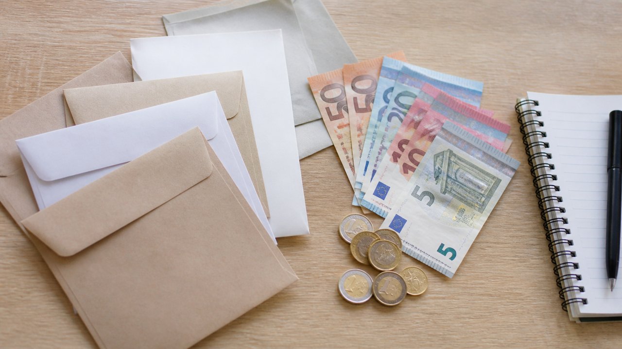 Ahşap masada zarflar, banknotlar ve küçük bir not defteri
